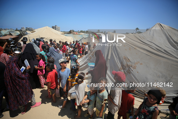 Displaced Palestinians are gathering to receive food cooked by a charity kitchen, amid food scarcity, as the Israel-Hamas conflict continues...