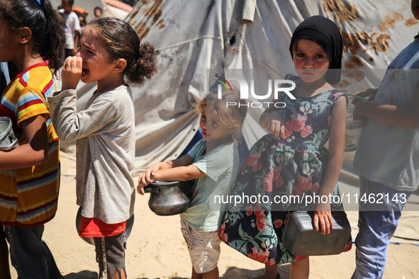 Displaced Palestinians are gathering to receive food cooked by a charity kitchen, amid food scarcity, as the Israel-Hamas conflict continues...