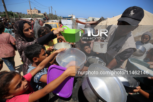 Displaced Palestinians are gathering to receive food cooked by a charity kitchen, amid food scarcity, as the Israel-Hamas conflict continues...