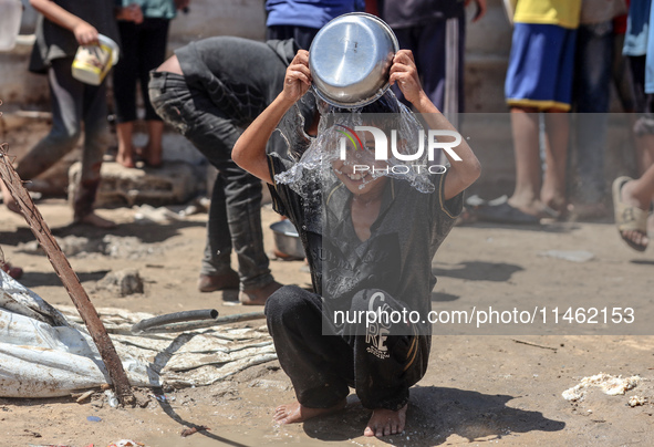 A displaced Palestinian boy is cooling himself with water outside his tent as Palestinians are gathering to receive food cooked by a charity...