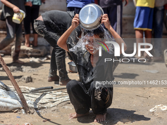 A displaced Palestinian boy is cooling himself with water outside his tent as Palestinians are gathering to receive food cooked by a charity...