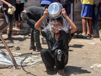 A displaced Palestinian boy is cooling himself with water outside his tent as Palestinians are gathering to receive food cooked by a charity...