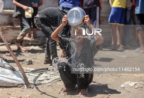 A displaced Palestinian boy is cooling himself with water outside his tent as Palestinians are gathering to receive food cooked by a charity...