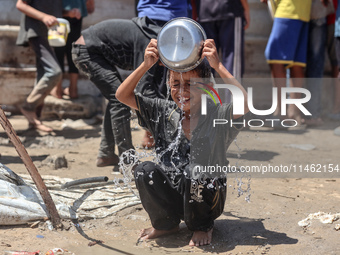 A displaced Palestinian boy is cooling himself with water outside his tent as Palestinians are gathering to receive food cooked by a charity...