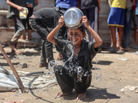 A displaced Palestinian boy is cooling himself with water outside his tent as Palestinians are gathering to receive food cooked by a charity...