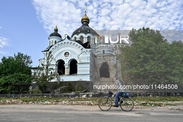 A man is riding a bicycle past the Church of the Nativity of the Blessed Virgin Mary, which was damaged by Russian shelling on July 8, in No...