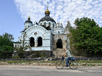 A man is riding a bicycle past the Church of the Nativity of the Blessed Virgin Mary, which was damaged by Russian shelling on July 8, in No...