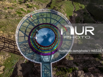 Tourists are experiencing a glass walkway at Pingding Mountain Scenic area in Mulei Kazak Autonomous county, Changji Hui Autonomous prefectu...