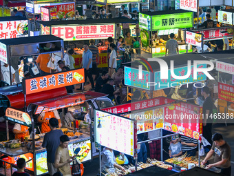 People are tasting food at the illuminated Longhu Zijin Night Market in Nanjing, China, on August 9, 2024. (