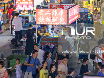 People are tasting food at the illuminated Longhu Zijin Night Market in Nanjing, China, on August 9, 2024. (