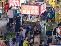 People are tasting food at the illuminated Longhu Zijin Night Market in Nanjing, China, on August 9, 2024. (