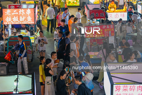 People are tasting food at the illuminated Longhu Zijin Night Market in Nanjing, China, on August 9, 2024. 