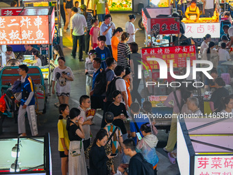 People are tasting food at the illuminated Longhu Zijin Night Market in Nanjing, China, on August 9, 2024. (