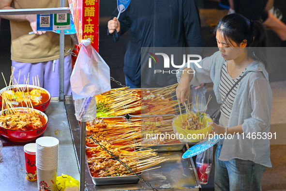 People are tasting food at the illuminated Longhu Zijin Night Market in Nanjing, China, on August 9, 2024. 