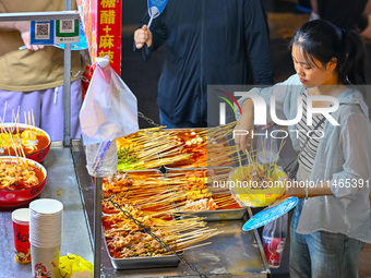 People are tasting food at the illuminated Longhu Zijin Night Market in Nanjing, China, on August 9, 2024. (