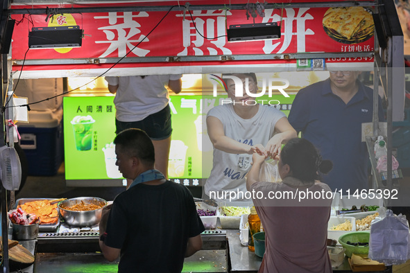 People are tasting food at the illuminated Longhu Zijin Night Market in Nanjing, China, on August 9, 2024. 