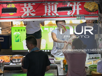 People are tasting food at the illuminated Longhu Zijin Night Market in Nanjing, China, on August 9, 2024. (