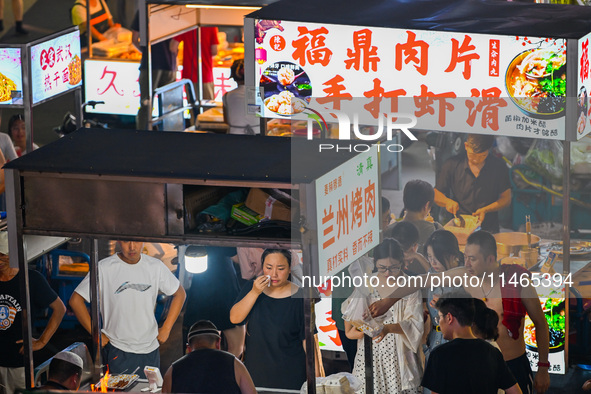 People are tasting food at the illuminated Longhu Zijin Night Market in Nanjing, China, on August 9, 2024. 