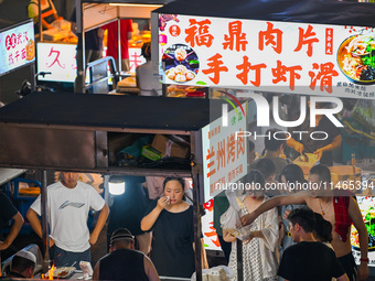 People are tasting food at the illuminated Longhu Zijin Night Market in Nanjing, China, on August 9, 2024. (