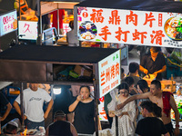 People are tasting food at the illuminated Longhu Zijin Night Market in Nanjing, China, on August 9, 2024. (