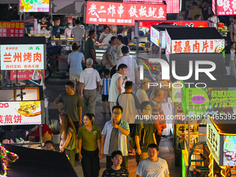 People are tasting food at the illuminated Longhu Zijin Night Market in Nanjing, China, on August 9, 2024. (