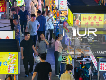 People are tasting food at the illuminated Longhu Zijin Night Market in Nanjing, China, on August 9, 2024. (