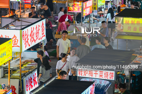 People are tasting food at the illuminated Longhu Zijin Night Market in Nanjing, China, on August 9, 2024. 