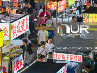 People are tasting food at the illuminated Longhu Zijin Night Market in Nanjing, China, on August 9, 2024. (