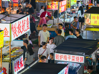 People are tasting food at the illuminated Longhu Zijin Night Market in Nanjing, China, on August 9, 2024. (