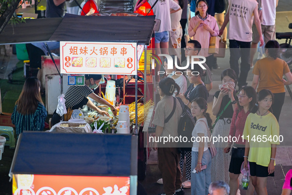 People are tasting food at the illuminated Longhu Zijin Night Market in Nanjing, China, on August 9, 2024. 