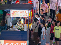 People are tasting food at the illuminated Longhu Zijin Night Market in Nanjing, China, on August 9, 2024. (