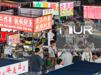 People are tasting food at the illuminated Longhu Zijin Night Market in Nanjing, China, on August 9, 2024. (