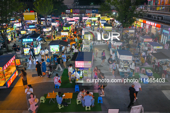 People are tasting food at the illuminated Longhu Zijin Night Market in Nanjing, China, on August 9, 2024. 