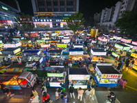 People are tasting food at the illuminated Longhu Zijin Night Market in Nanjing, China, on August 9, 2024. (