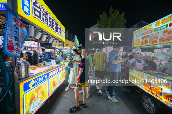 People are tasting food at the illuminated Longhu Zijin Night Market in Nanjing, China, on August 9, 2024. 