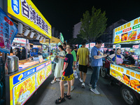 People are tasting food at the illuminated Longhu Zijin Night Market in Nanjing, China, on August 9, 2024. (