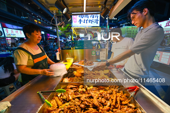 People are tasting food at the illuminated Longhu Zijin Night Market in Nanjing, China, on August 9, 2024. 