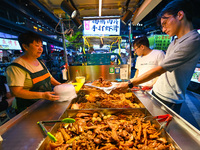 People are tasting food at the illuminated Longhu Zijin Night Market in Nanjing, China, on August 9, 2024. (