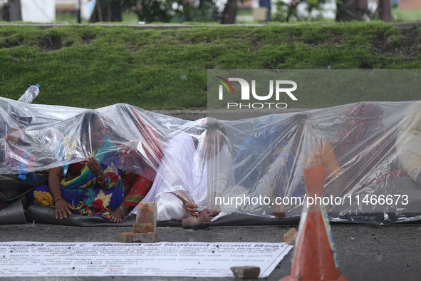 A group of human rights activists are taking shelter under plastic sheets as it is raining heavily during a sit-in protest in Kathmandu, Nep...