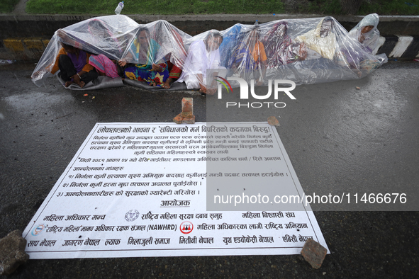 A group of human rights activists are taking shelter under plastic sheets as it is raining heavily during a sit-in protest in Kathmandu, Nep...