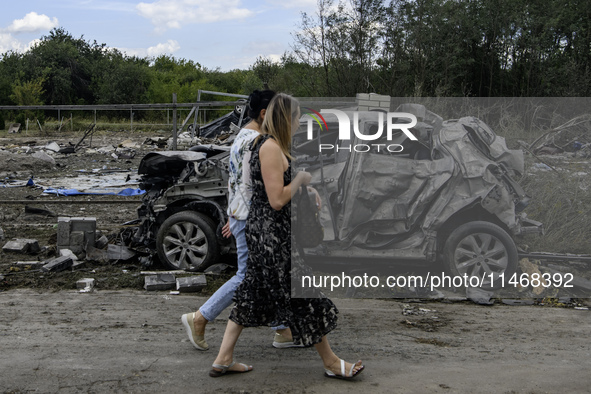 Local women are walking next to a destroyed car in a village in the Kyiv region, Ukraine, on August 11, 2024, heavily damaged during a massi...