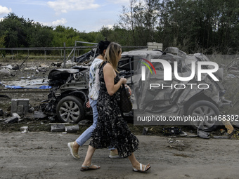 Local women are walking next to a destroyed car in a village in the Kyiv region, Ukraine, on August 11, 2024, heavily damaged during a massi...