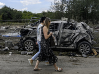 Local women are walking next to a destroyed car in a village in the Kyiv region, Ukraine, on August 11, 2024, heavily damaged during a massi...