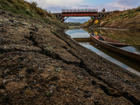 A biker is moving over an iron bridge as the level of water bodies has decreased, leaving boats on the shores and triggering a drought-like...