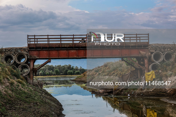 A biker is moving over an iron bridge as the level of water bodies has decreased, leaving boats on the shores and triggering a drought-like...