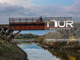 A biker is moving over an iron bridge as the level of water bodies has decreased, leaving boats on the shores and triggering a drought-like...