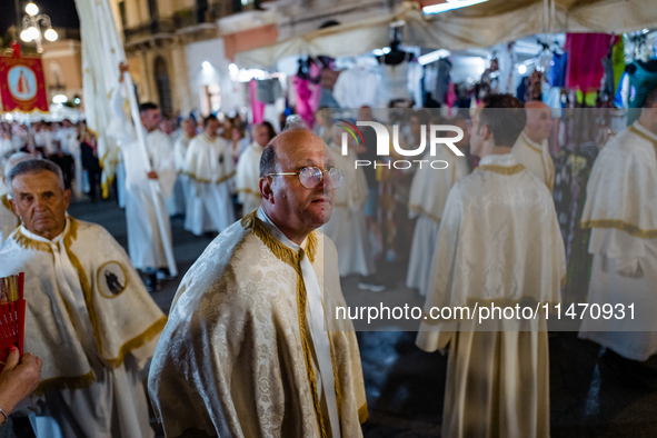 A member of the confraternity is participating in the procession of the statue of the Three Saints of Bisceglie among the stalls set up for...