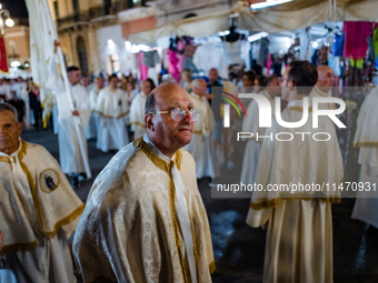 A member of the confraternity is participating in the procession of the statue of the Three Saints of Bisceglie among the stalls set up for...