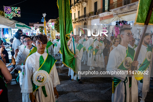 Members of the confraternity are processing the statue of the Three Saints of Bisceglie among the stalls set up for the festival in the town...