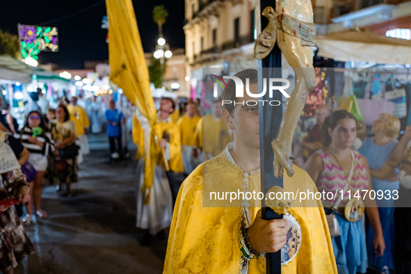 A member of the confraternity is participating in the procession of the statue of the Three Saints of Bisceglie among the stalls set up for...